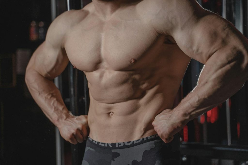 Detailed image of a muscular male torso flexing in a gym setting, emphasizing strength.